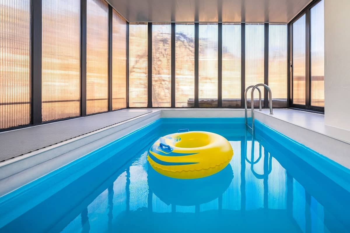 An indoor swimming pool with clear blue water, a yellow inflatable ring, and a metal ladder.