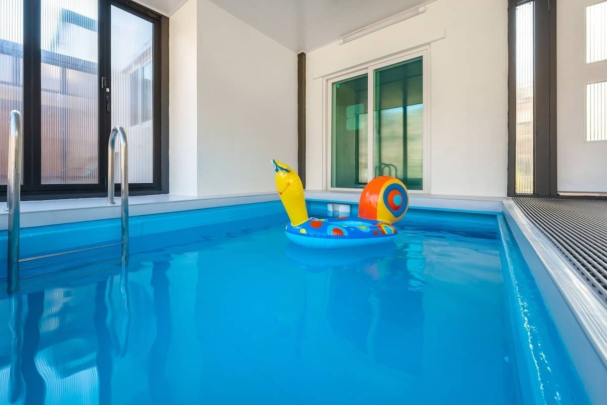 An indoor swimming pool with clear blue water, a metal ladder, and colorful inflatable toys.