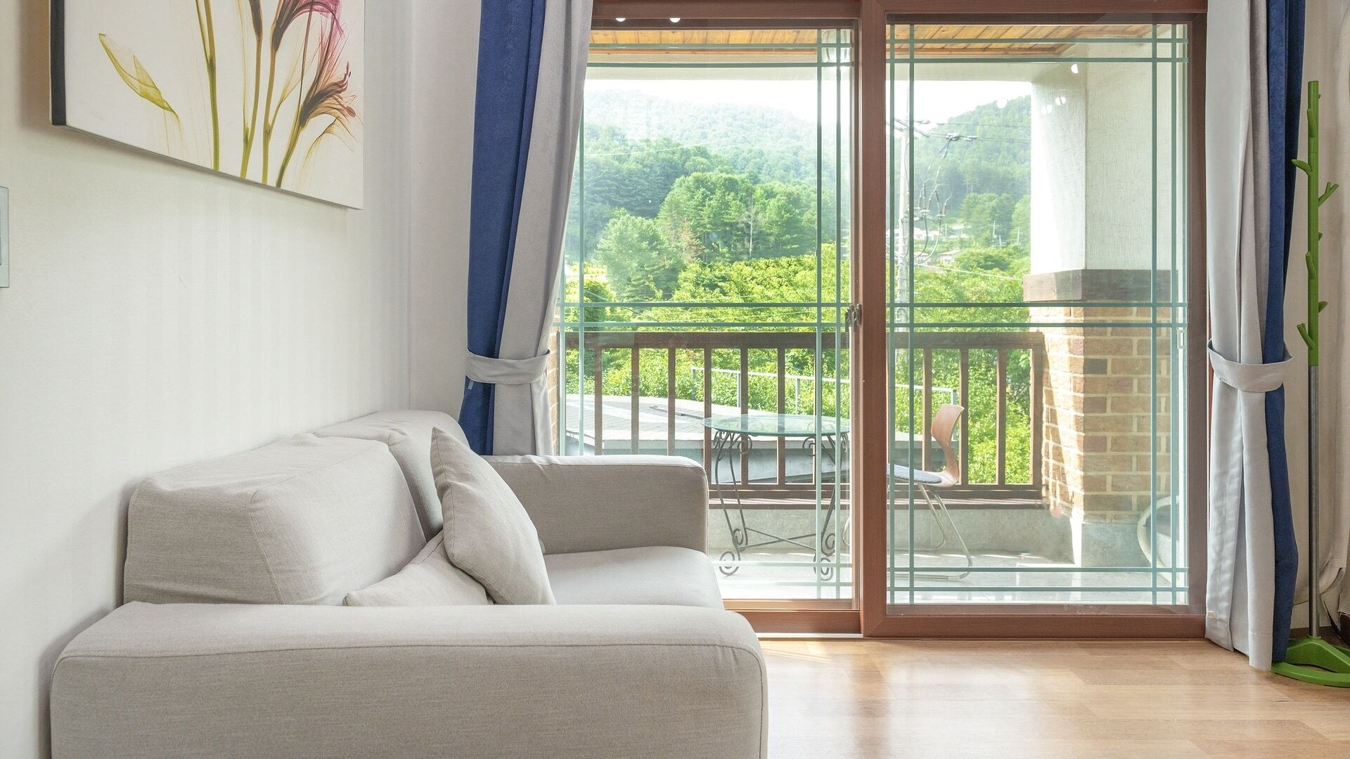 Ein Zimmer mit einer Couch, einer Glastür, die auf einen Balkon mit Tisch und Stühlen führt, und einem Gemälde an der Wand.