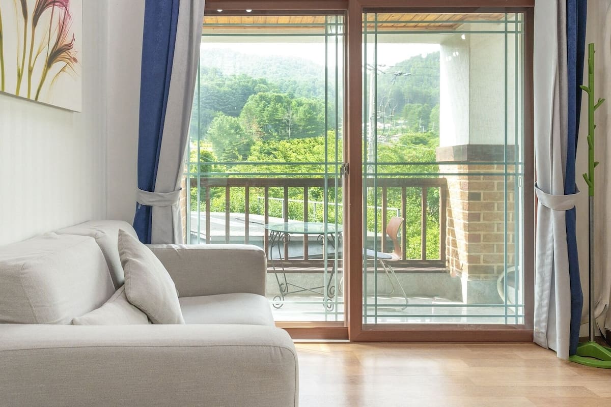 A room with a sofa, a glass door leading to a balcony with a table and chairs, and a painting on the wall.