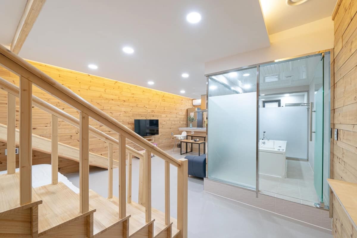 A modern interior with a wooden staircase, a kitchen area, and a glass-enclosed shower.