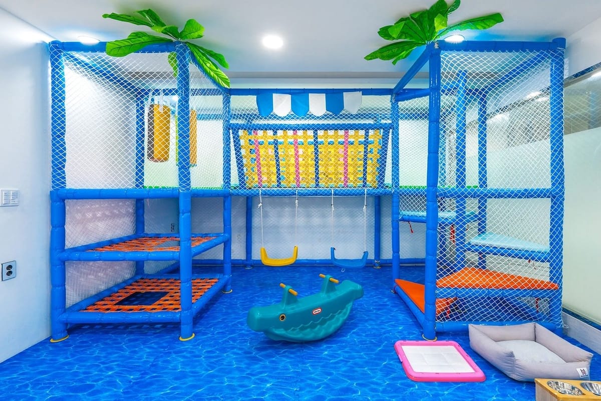 A children's play area with a pool, slides, and a netted climbing structure.