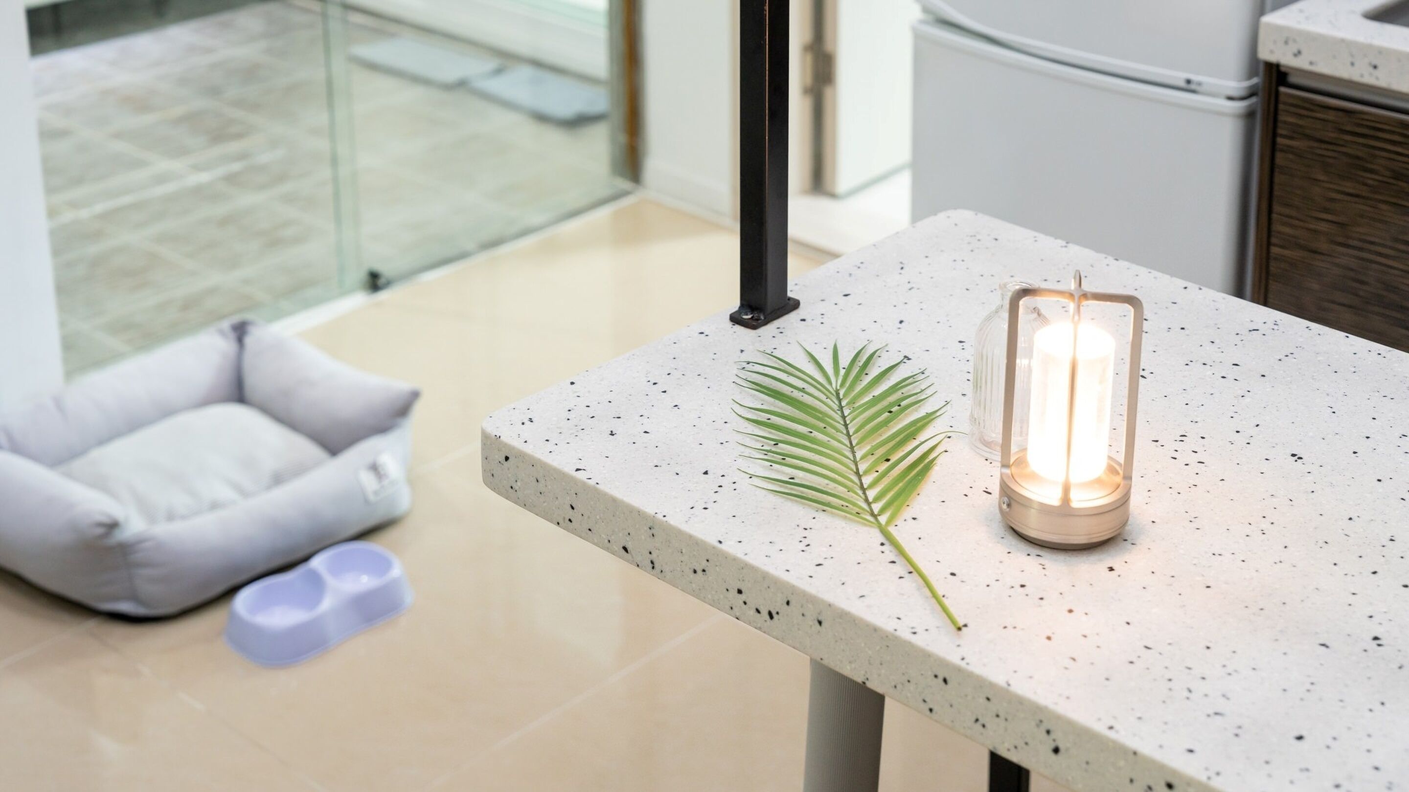 A modern kitchen with a concrete countertop, a hanging light fixture, and a pet bed.