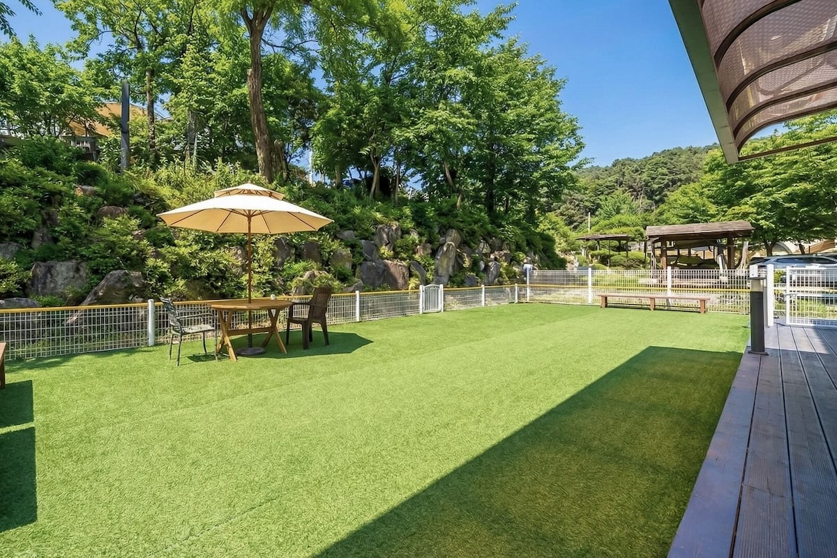 Un espace extérieur bien entretenu, doté d’une pelouse artificielle, d’une table en bois avec des chaises, d’un banc et d’une structure en forme de pergola.