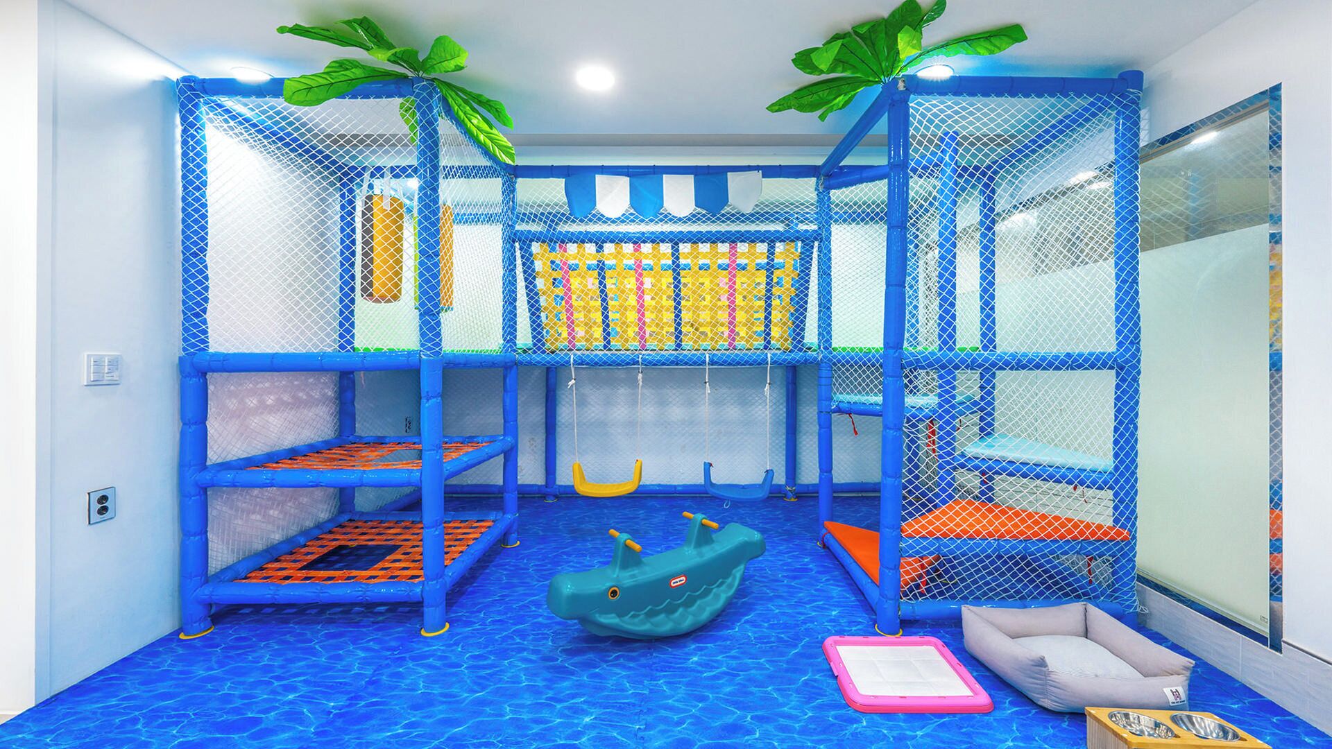 A play area with a blue net structure, a slide, a small boat, and a soft play mat.