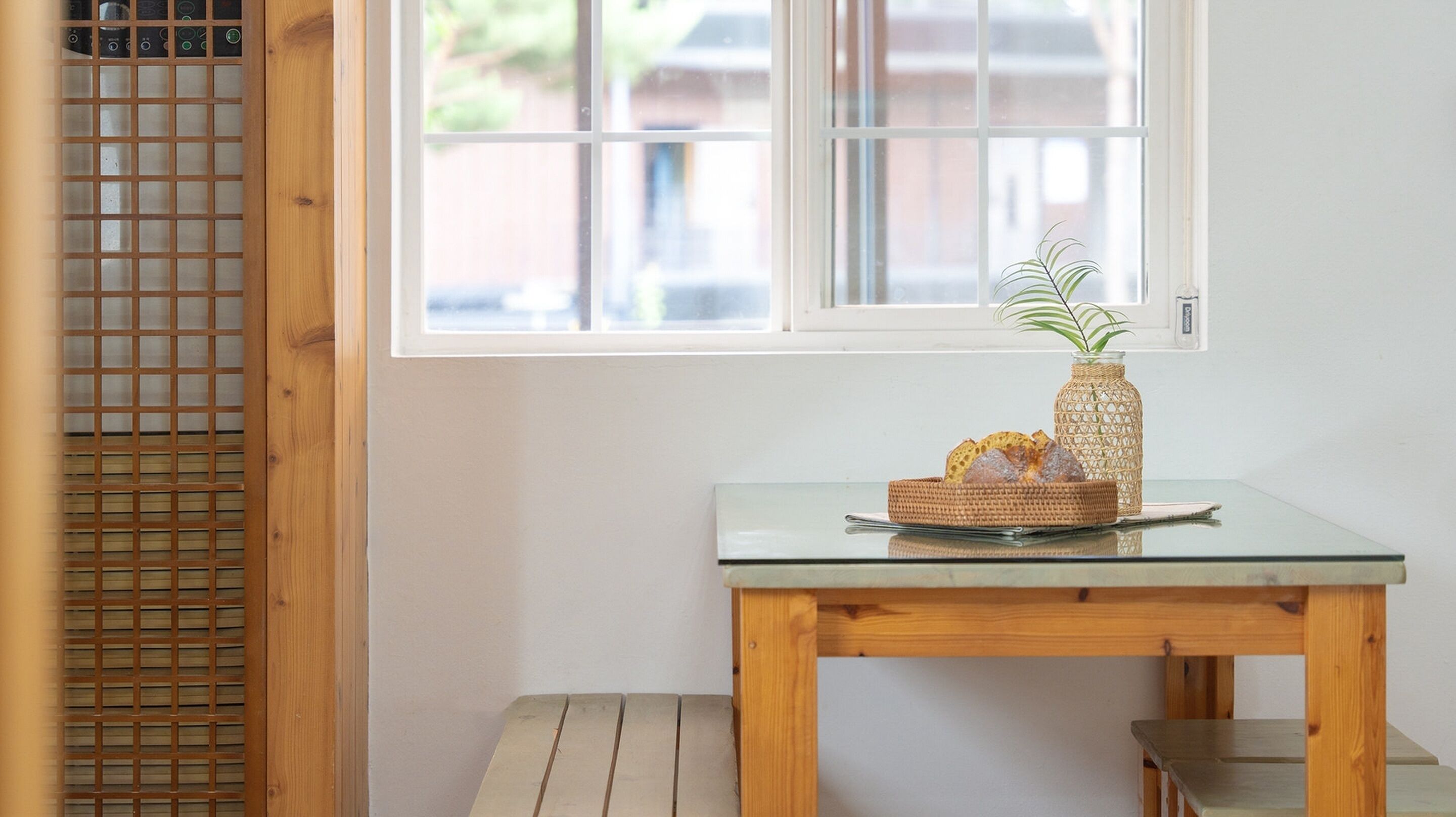 A small wooden table with a glass top, a wicker basket with bread, and a glass vase with a plant.