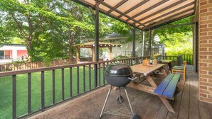 A covered outdoor patio with a barbecue grill, wooden tables and benches, and a view of a green lawn and trees. - Gapyeong Himong Aegyeon Kids Pension (Gapyeong)