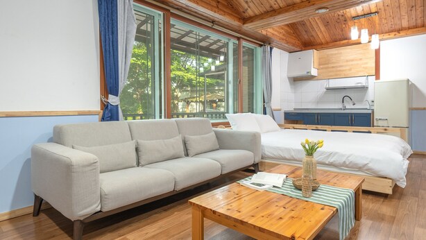 A modern room with a sofa, a bed, a wooden coffee table, and a view of greenery outside. - Gapyeong Himong Aegyeon Kids Pension (Gapyeong)
