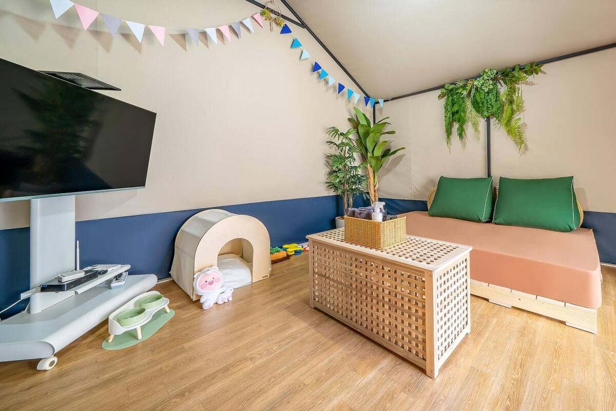 A cozy living room with a TV, a sofa, a playpen, and a small table with a plant.