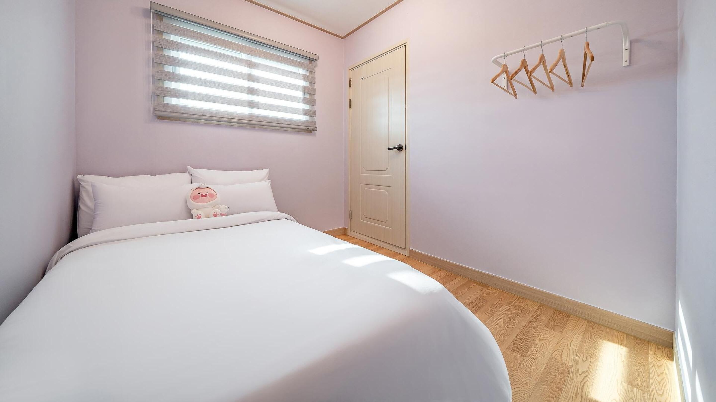 A bedroom with a bed, a window with blinds, a door, and a wall-mounted drying rack.