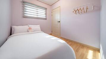 A bedroom with a bed, a window with blinds, a door, and a wall-mounted drying rack.