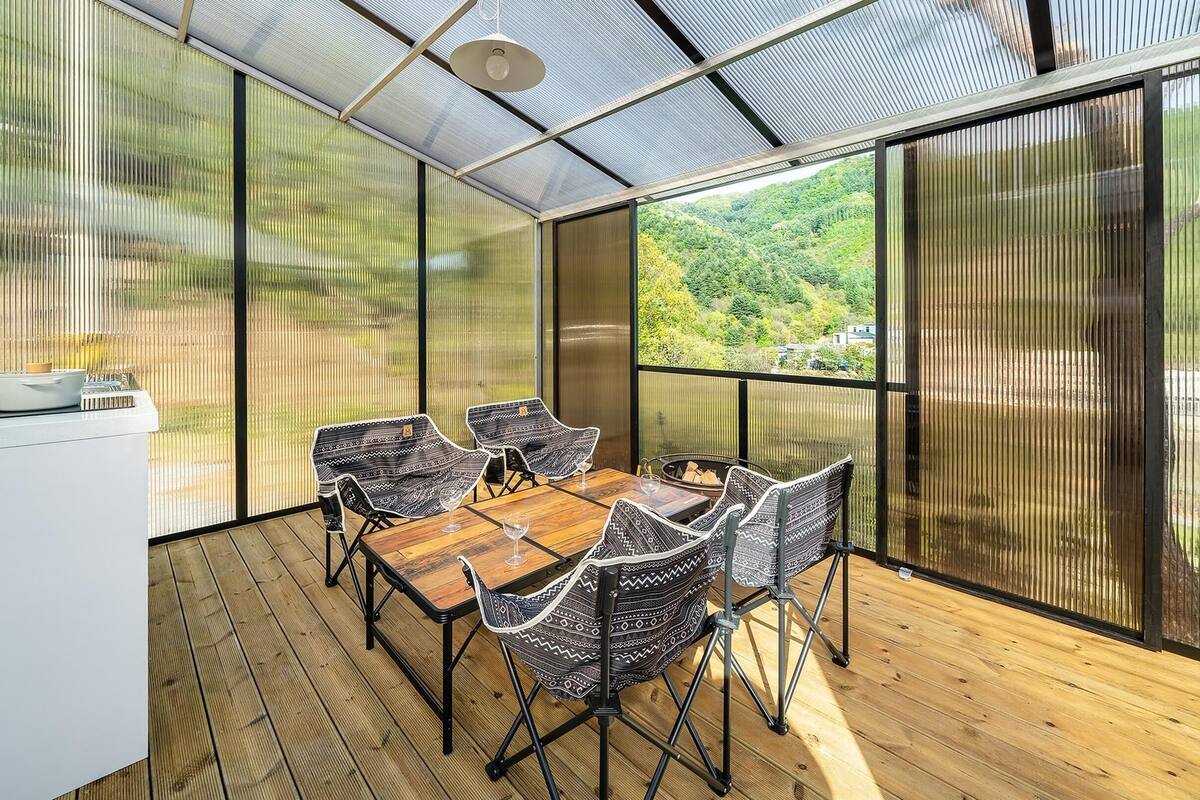 A modern kitchen with a wooden table and chairs, large windows with a view of greenery, and a ceiling with a mesh design.