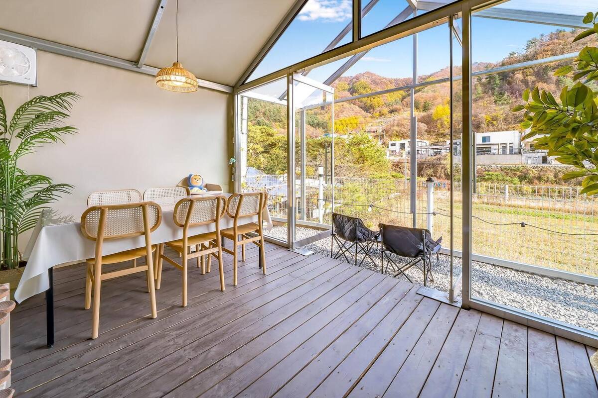 A wooden deck with a table and chairs, large windows offering a view of a hilly landscape, and a hanging light fixture.