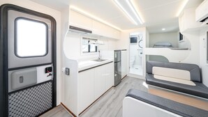 Interior compacto de una caravana con kitchenette, un baño pequeño y una zona de dormir con literas.