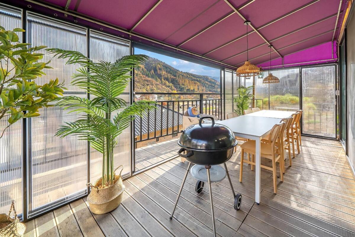 A balcony with a grill, dining table, chairs, and potted plants.
