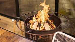 A fire pit with logs burning, surrounded by a metal frame, set on a wooden floor. - Gapyeong Ddobagi Pet & Spa Glamping (Gapyeong)