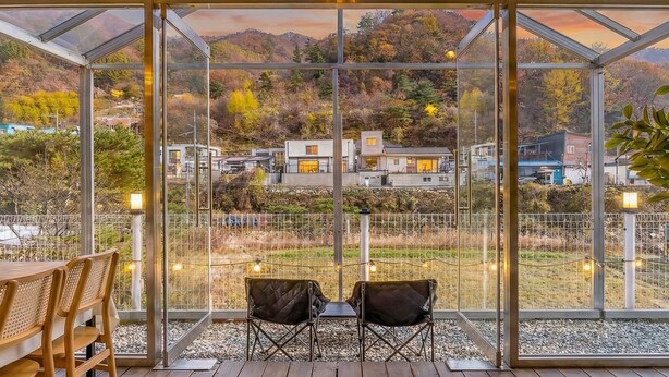Un invernadero con vistas a una zona residencial, dos sillas y una mesa.