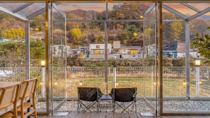 A conservatory with a view of a residential area, two chairs, and a table. - Gapyeong Ddobagi Pet & Spa Glamping (Gapyeong)