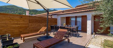 Un patio con mobiliario de madera, una mesa con sillas y un paraguas grande.