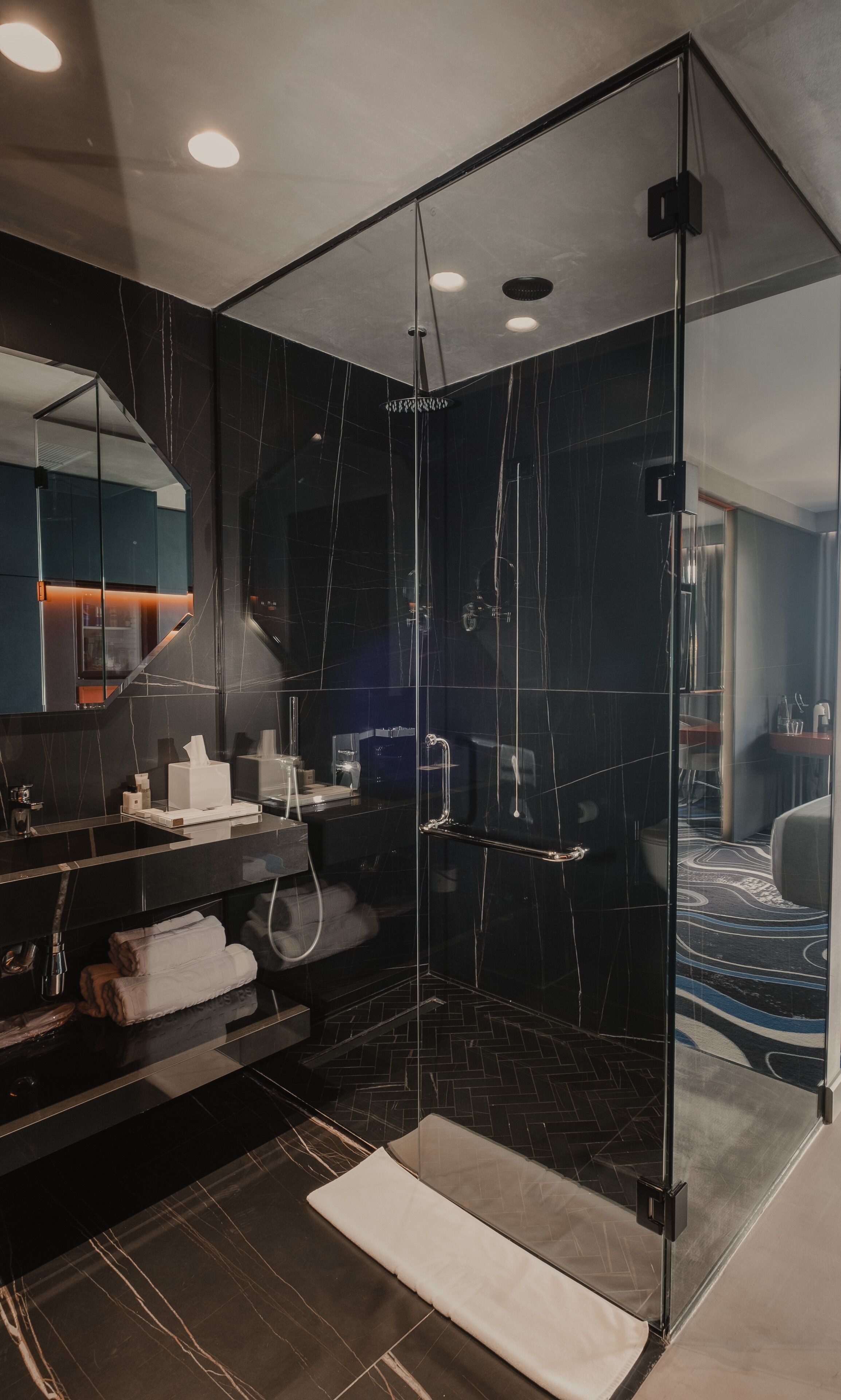 Un baño moderno con cabina de ducha de vidrio, baldosas de mármol oscuro y un mueble de tocador con espejo y toallero.