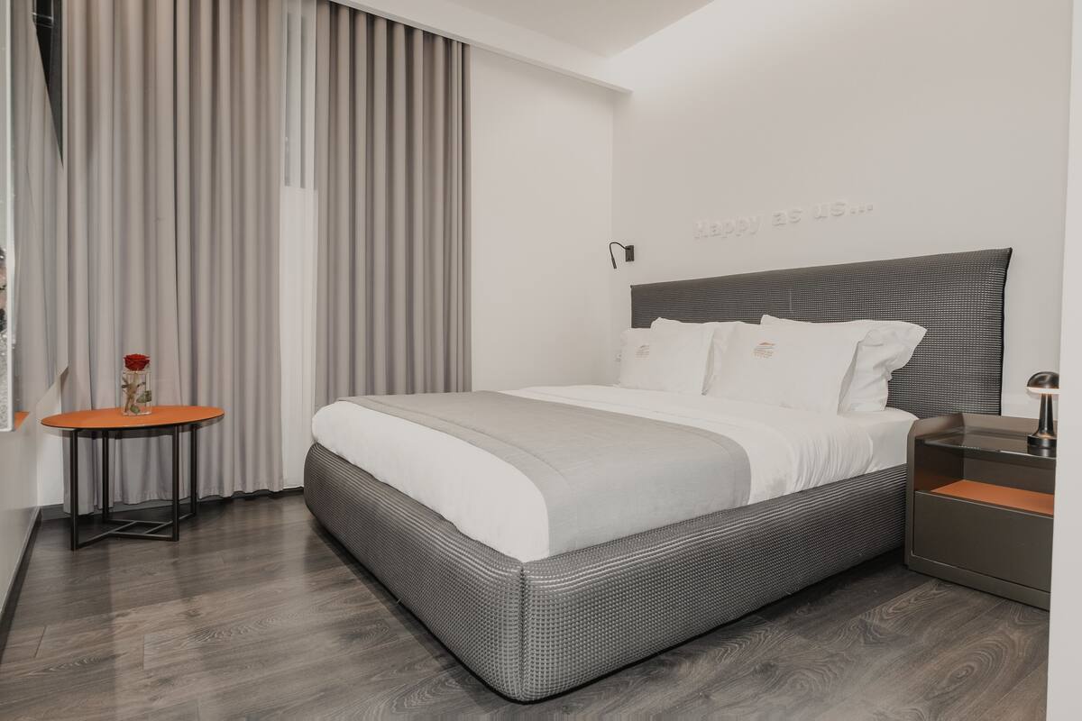 Ein modernes Hotelzimmer mit einem großen Bett, einem kleinen Tisch und einem Nachttisch.
