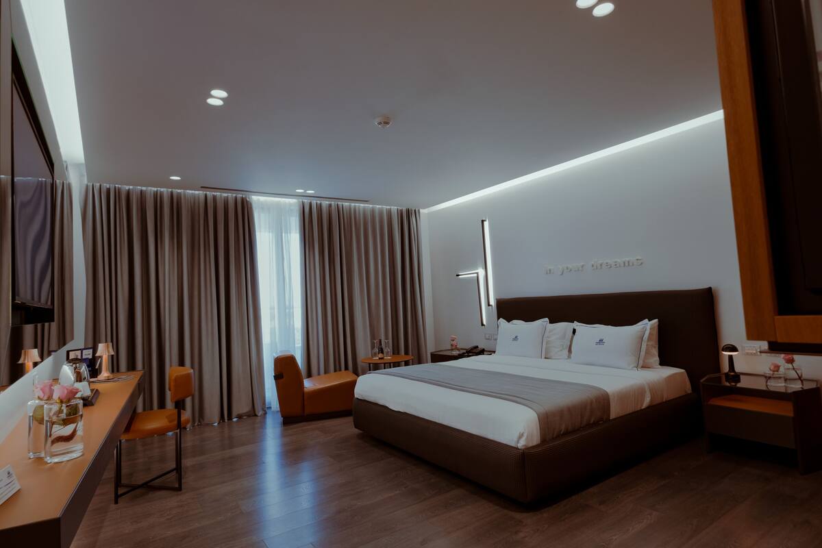Ein modernes Hotelzimmer mit einem großen Bett, einem Schreibtisch mit Stuhl, einem kleinen Tisch und einem Fernseher.
