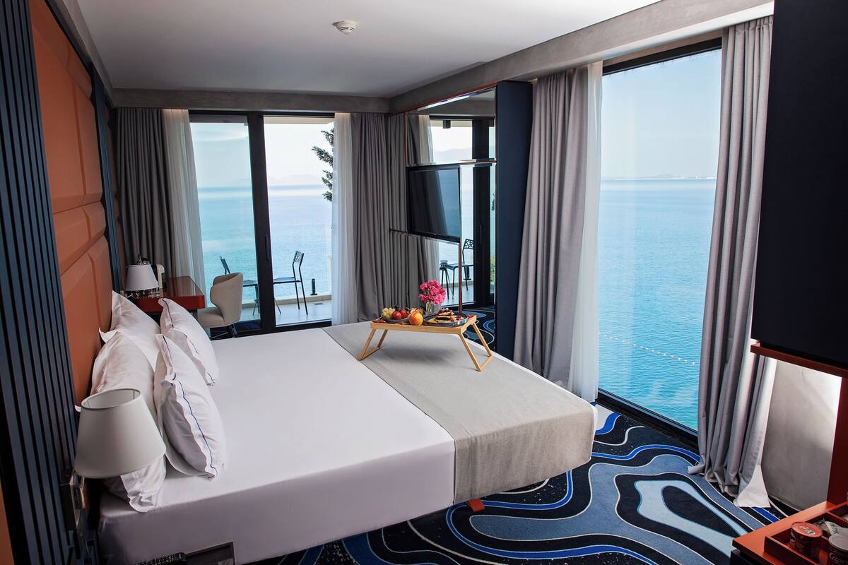 Ein Hotelzimmer mit einem großen Bett, einem Fernseher, einem kleinen Tisch mit Obst und Blick aufs Meer.