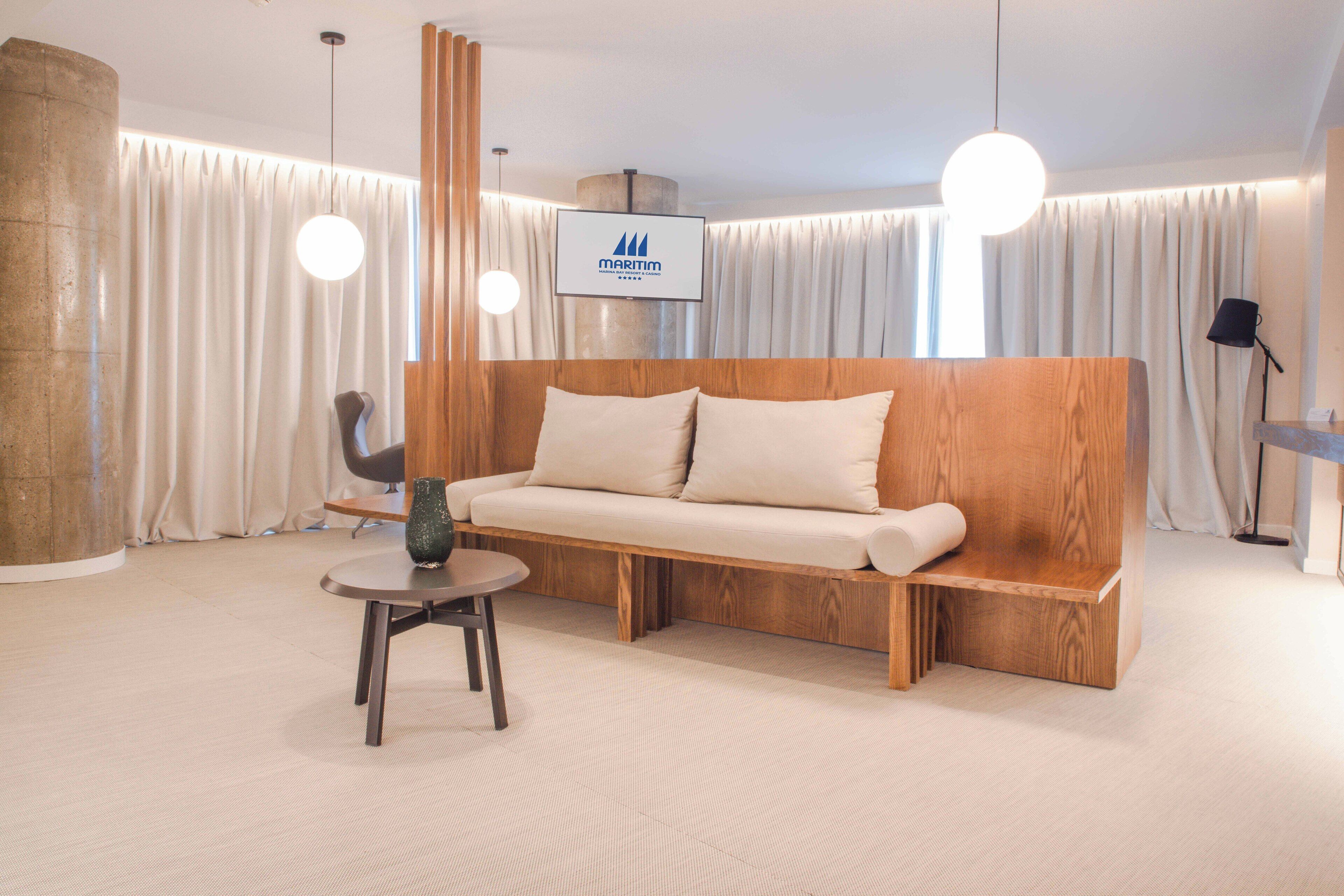 A modern hotel lobby with a wooden sofa, a small round table, and a TV screen displaying the brand name.