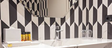 A bathroom with a black and white geometric tile backsplash, a white marble sink, a mirror, and neatly folded towels.