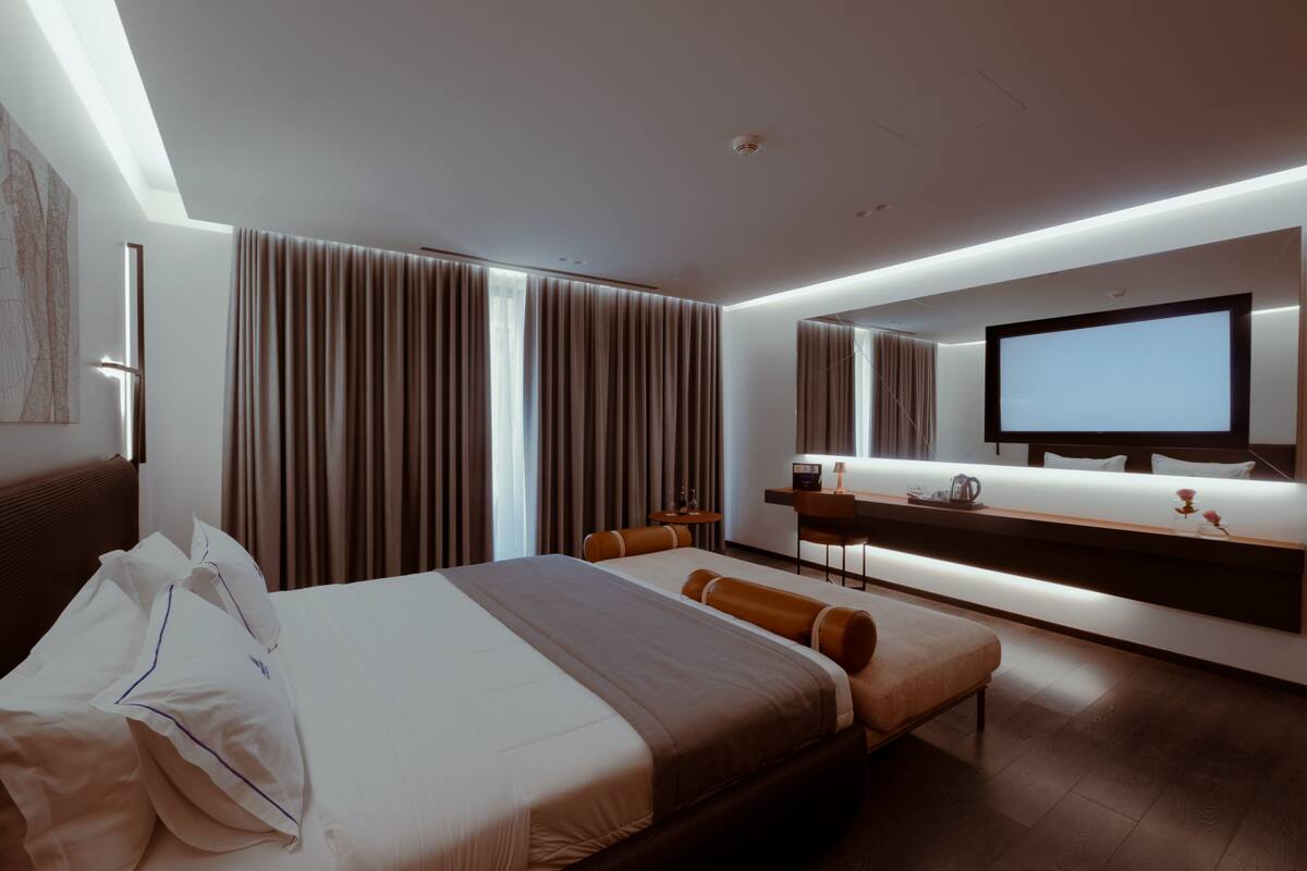 Ein modernes Hotelzimmer mit einem großen Bett, einem Schreibtisch, einem Flachbildfernseher und einem großen Fenster mit Vorhängen.