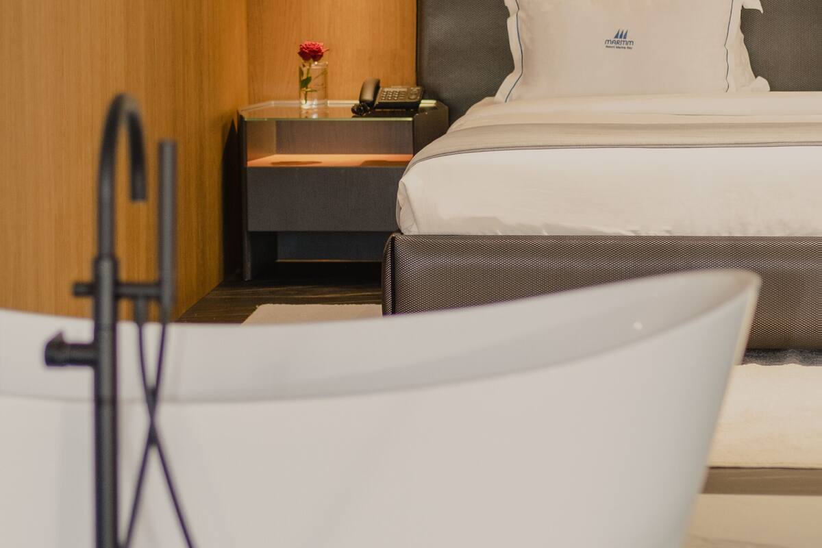 Ein Hotelzimmer mit Holzwand, einem Bett mit weißer Bettwäsche, einem Nachttisch mit Telefon und einem kleinen Tisch mit Blumenvase.