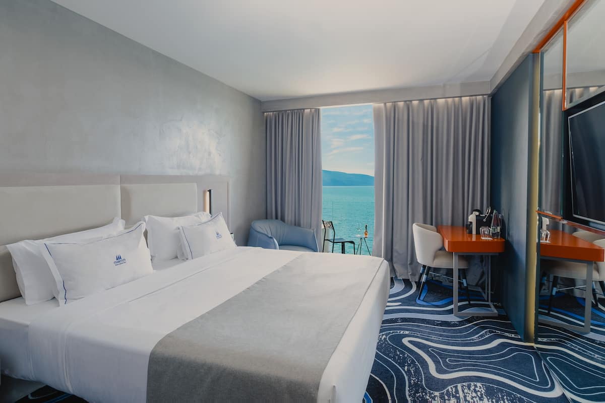 Ein Hotelzimmer mit einem großen Bett, einem Schreibtisch, einem Stuhl und Blick aufs Meer.