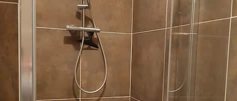 A glass-enclosed shower with a handheld showerhead and a wall-mounted control panel.