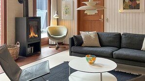 Ein Wohnzimmer mit Kamin, einer Couch, einem Sessel, einem runden Tisch und einer Pendelleuchte.