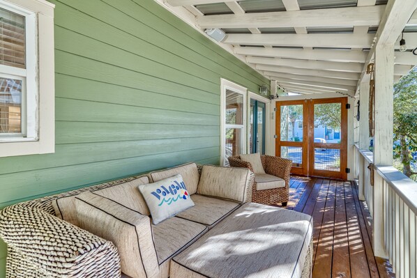 A covered porch with a green exterior, wicker furniture, and a view of the street.