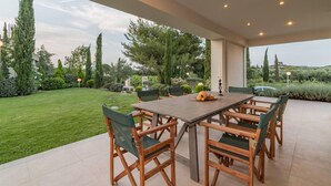 An outdoor patio with a wooden table and chairs, surrounded by a well-maintained garden and trees.