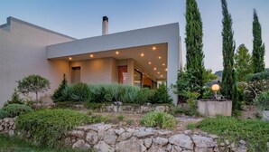A modern house with a stone retaining wall, a well-maintained garden, and a clear sky.
