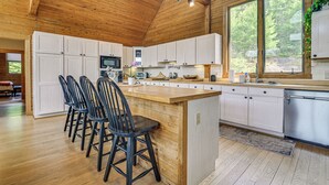 Une cuisine spacieuse avec des meubles en bois, un îlot central doté de tabourets de bar et de grandes fenêtres offrant une vue sur l’extérieur.