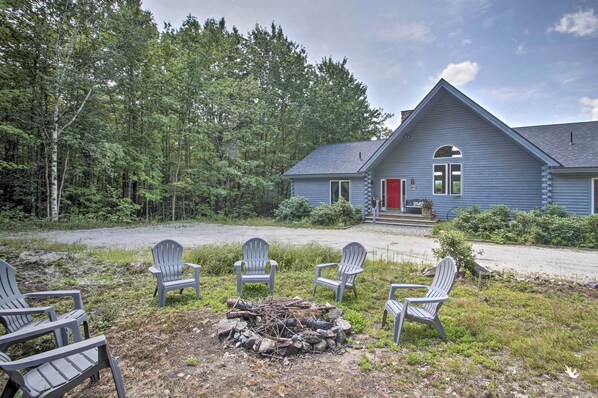 A cabin with a fire pit and Adirondack chairs in front.