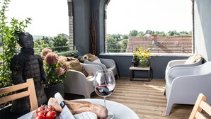 A terrace with a statue, seating, a table with bread, tomatoes, cheese, and a wine glass.