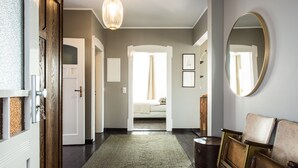 A hallway with a dark wooden floor, a green rug, a wooden bench, and a large mirror on the wall.
