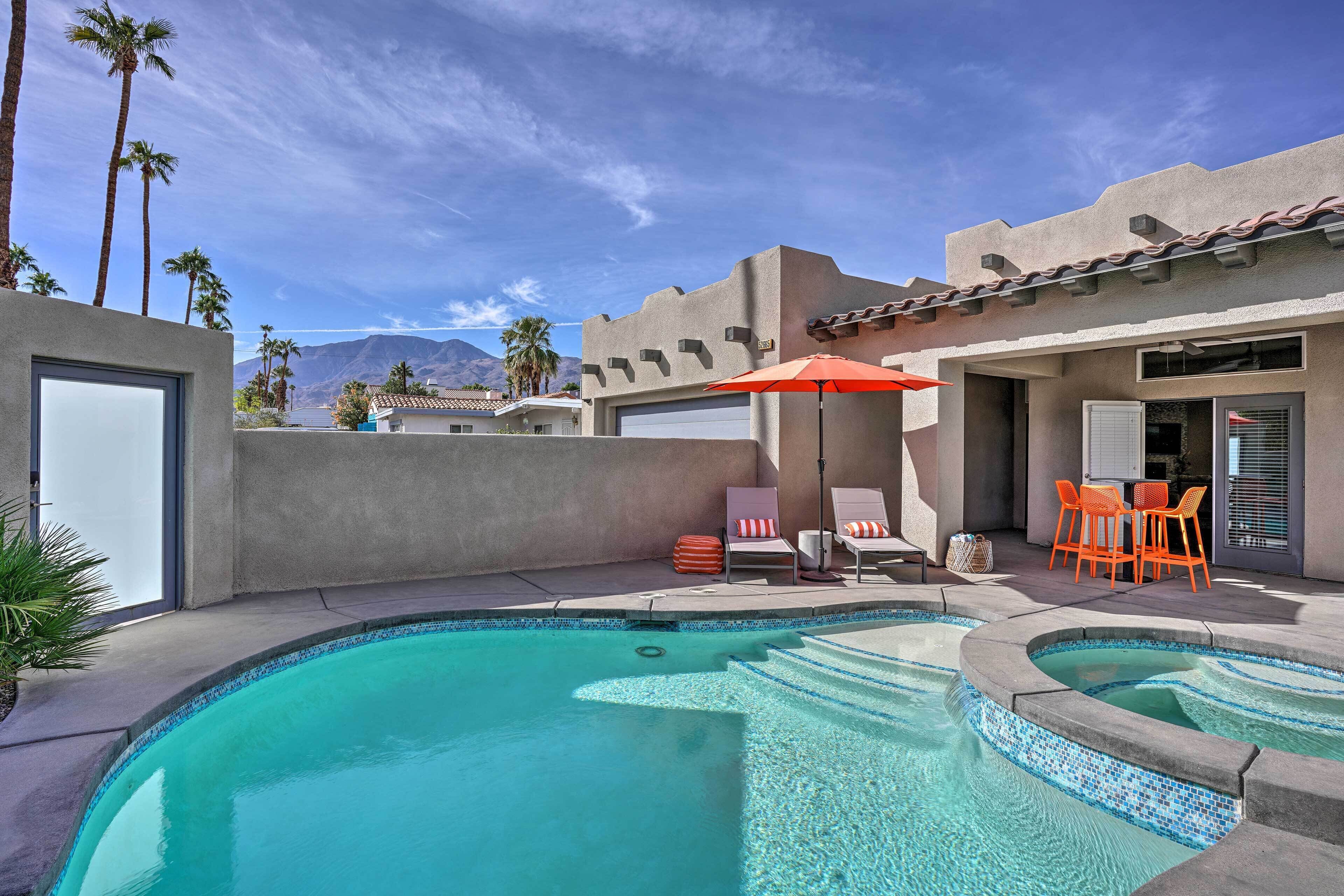 A swimming pool with a tiled edge, surrounded by lounge chairs and an umbrella.