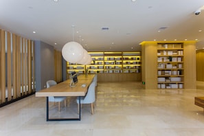 A modern library with a long wooden table, multiple chairs, and bookshelves.
