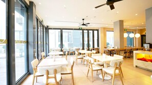 A modern dining area with tables and chairs, large windows, and a ceiling fan.