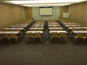 A conference room with rows of tables and chairs, a projector screen, and a whiteboard.