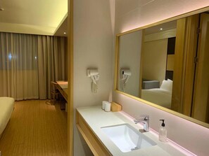 A hotel room with a wooden floor, a white sink with a mirror, a hairdryer, and a wooden bench.