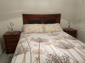 A neatly made bed with floral bedding, a wooden headboard, and two bedside tables with lamps. - Live in Paradise (Marbella)
