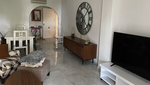 A living room with a TV, a large wall clock, and a dining area with a table and chairs. - Live in Paradise (Marbella)