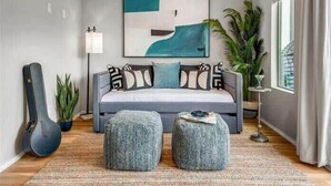 A modern bedroom with a grey sofa, two ottomans, a guitar, and a large abstract painting on the wall. - New, Luxury Home| Private Roof Deck (Nashville)
