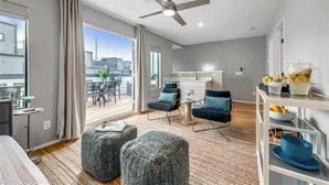 A modern living room with a sofa, ottomans, a ceiling fan, and a dining area with chairs. - New, Luxury Home| Private Roof Deck (Nashville)